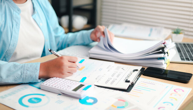 Business professional reviewing financial documents, writing notes, and analyzing business data on a laptop at a desk, representing financial planning