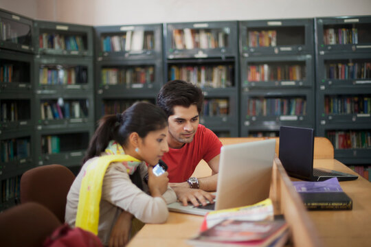 College students looking at laptop in library