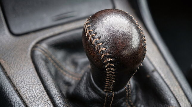 Close-up of a worn leather-wrapped gear shift knob with stitching in a car interior