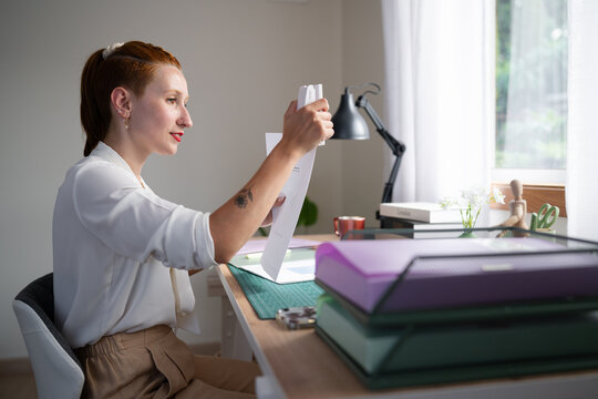 A white woman staples papers while working from home in Galicia, spain