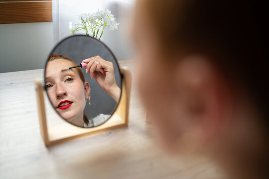 A white woman applies mascara looking