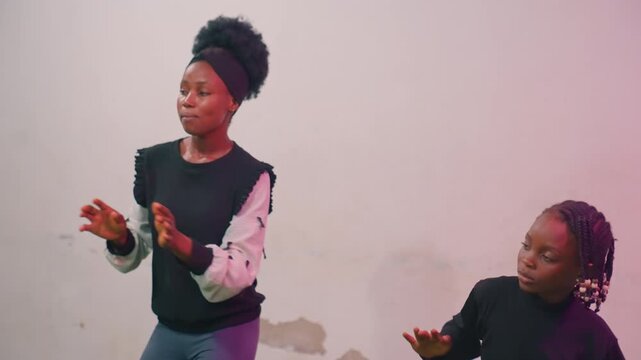 Black mother and child gesturing together in studio with coordinated hand choreography mother acting as storyteller and signlike coach while child mirrors expressive motions, warm pink light