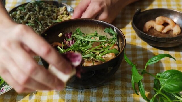 Preparing healthy dinner or breakfast. Female hand adding arugula and lettuce to summer salad