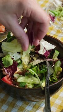 Vertical video. Preparing healthy dinner or breakfast. Female hand adding lettuce to summer salad