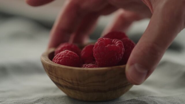 Slow motion man hand put fresh ripe raspberries in a small wooden bowl