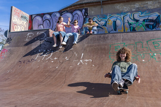 A teenage girl rides a skateboard down a ramp at an outdoor skatepark