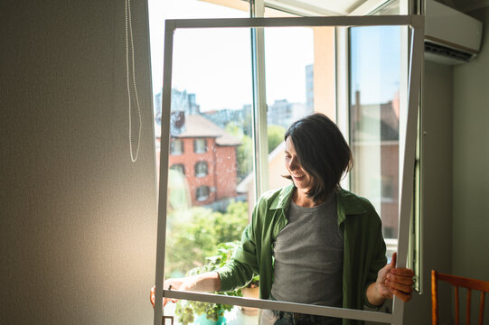Smiling homeowner installing mosquito net on window indoors