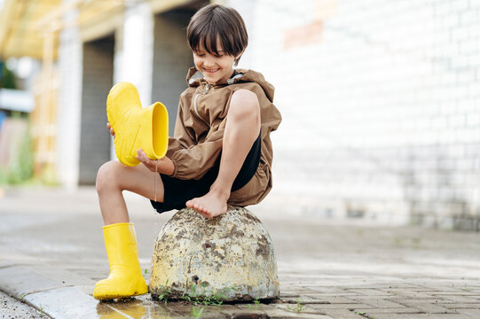 Smiling boy pours water from his yellow rubber boot