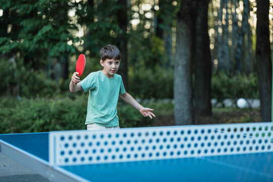 A focused boy plays table tennis outside in the green summer park