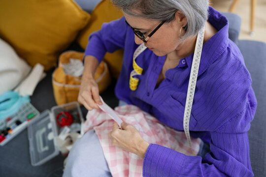 Mature individual sewing fabric at home wearing glasses and measure tape