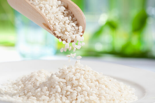 Rice grains pouring from wooden scoop, close up