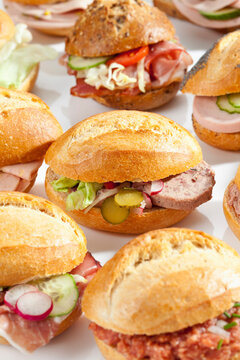 Variety of bread rolls sandwiches with mixed cold cuts on white background, close up