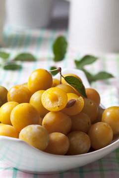 Mirabelles (Prunus domestica subsp. syriaca) in a bowl on wooden table, studio shot