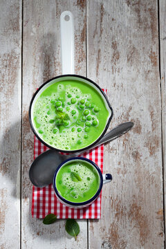 Saucepan and mug of pea soup, spoon and cloth on wood