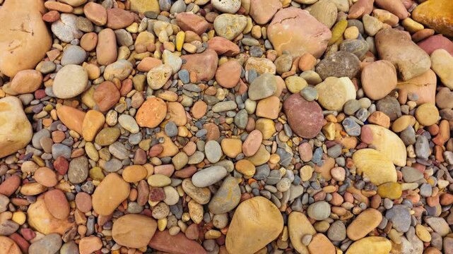 Smooth multicolored beach pebbles in close top view with red, yellow, gray and brown tones. Natural rounded stones across dry ground. Coastal rock texture for geology, nature and abstract background