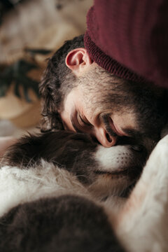 A smiling young man cuddles affectionately with his dog indoors