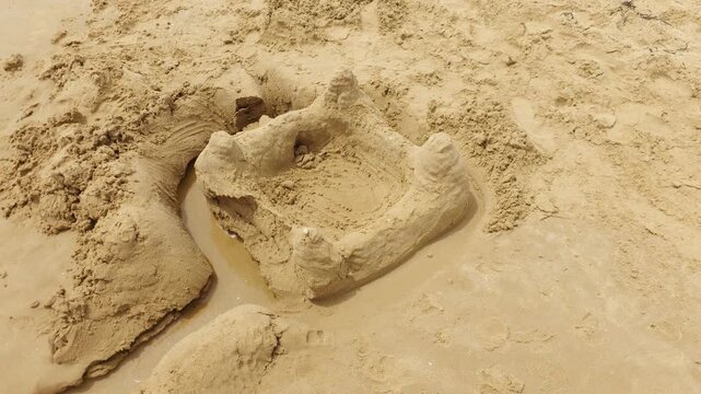 Sand castle on wet beach with handmade towers and moat after children playing. Simple sand sculpture near shoreline. Summer vacation, family recreation and creative seaside activity