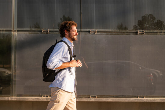 Smiling businessman with backpack walks by a red wall outdoors