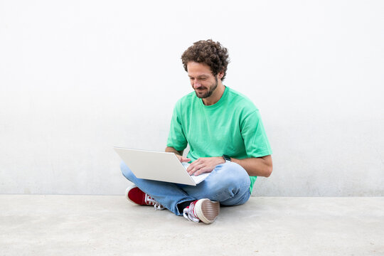 Smiling male in green shirt sits cross-legged using laptop