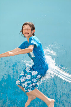 Germany, Boy jumping in splash of water against blue background