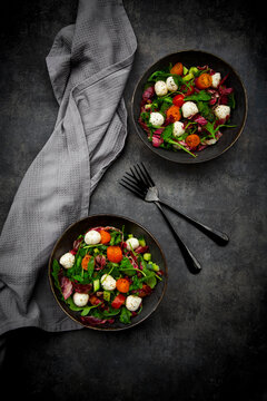 Two bowls feature fresh mozzarella salad on dark concrete
