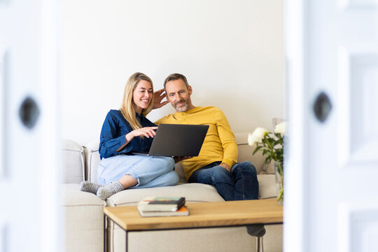 Smiling man and woman sit on sofa indoors and browse laptop