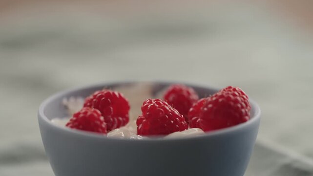 Slow motion man hand add ripe raspberries to yogurt in a bowl