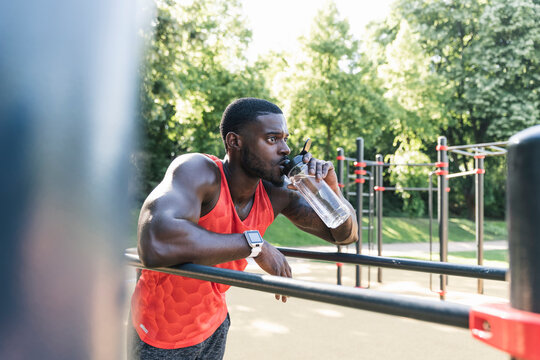 Young athlete training on parallel bars, outdoors, drinking water