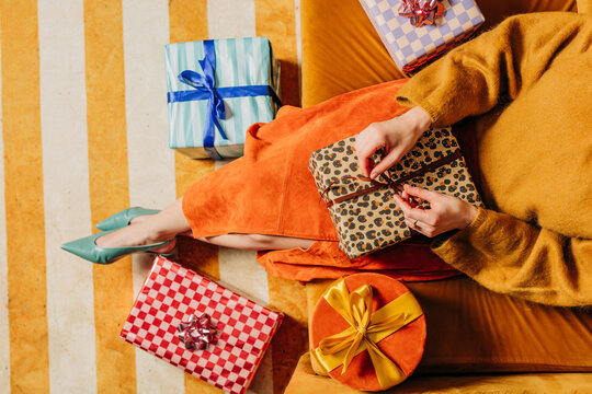Stylish woman unwraps a Christmas gift on a couch indoors