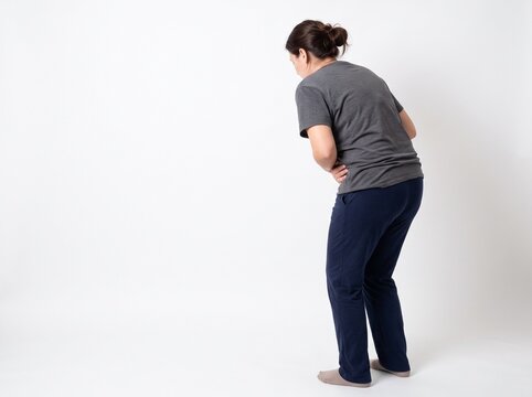 Woman with bloating and stomach ache from overeating seen from back angle, isolated on white background	