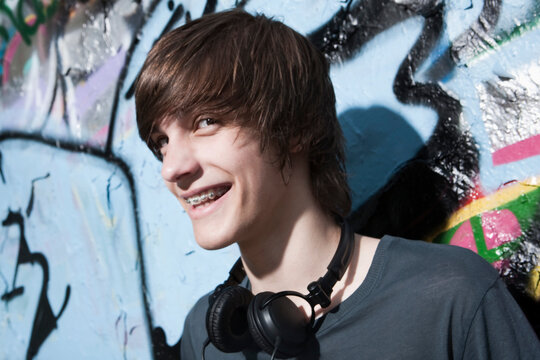 Teenage boy with headphone smiles near a graffiti wall in Berlin