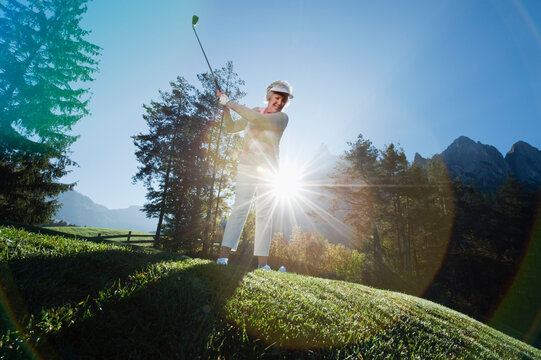 A woman swings a golf club on a sunny outdoor course in Italy