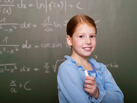 Girl (6-7) standing by blackboard, smiling, portrait, close-up