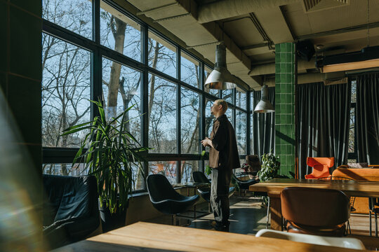 Businessman stands in modern coworking space looking at window