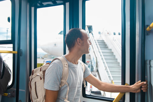 Man with backpack stands in airport bus looking at aircraft