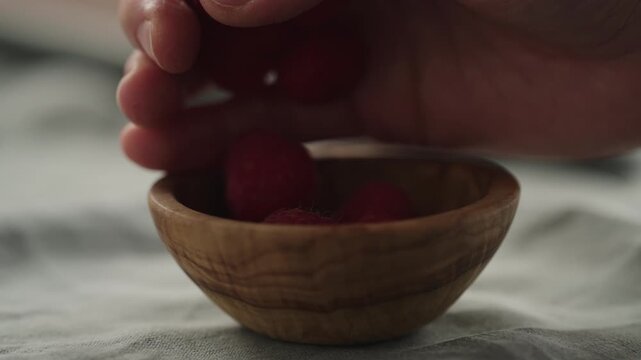 Slow motion man hand put fresh ripe raspberries in a small wooden bowl