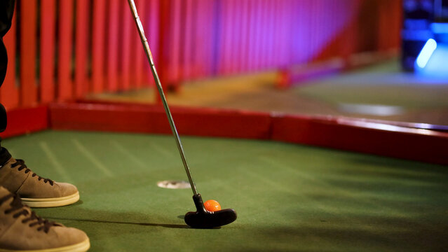 Close-Up of Player Preparing to Putt Orange Ball in Mini Golf