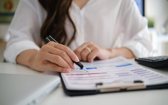 Young Asian businesswoman reviewing and marking financial reports at her office desk.