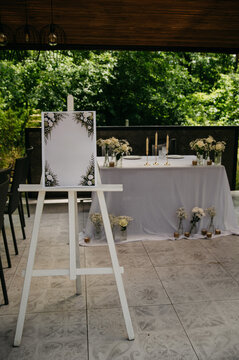 Interior of an open-air restaurant for a wedding or anniversary celebration with a blank seating chart standing on a white tripod