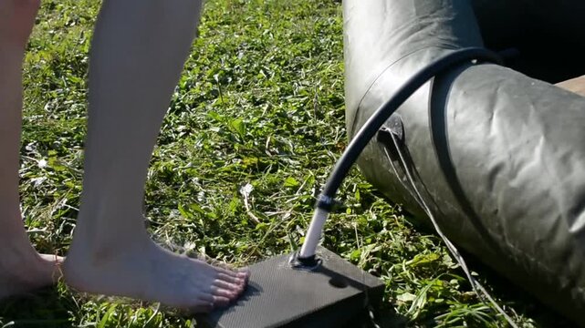 Woman inflating a rubber boat using a foot pump. Person standing barefoot on a floor pump to fill an inflatable raft with air for outdoor recreational water sport.