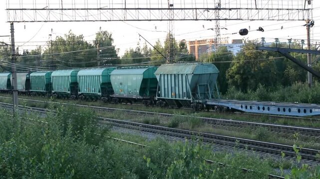 Freight train with green cargo hopper cars moving along railway tracks in countryside. Industrial logistics transport system on railroad during sunny summer day.