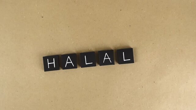 Top down view showing the word halal, representing Islamic dietary law and permissible food for Muslims, spelled out with black letter tiles on a brown recycled paper background