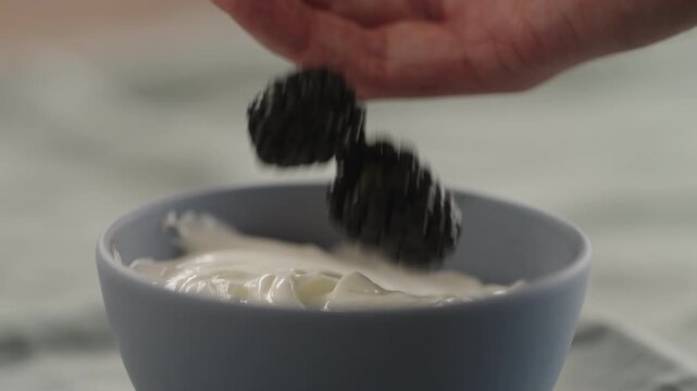 Slow motion man hand add ripe blackberries to yogurt in a bowl