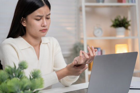 Asian young woman working in office with a carpal tunnel syndrome or wrist joint inflammation, hand muscle inflammation from office syndrome , hand muscle pain from working