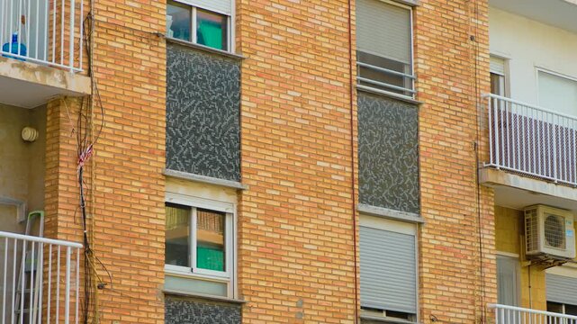 Brick apartment building in Spain with window barriers and closed roller shutters. Residential facade with protective metal rails. Property security against illegal occupation and squatting