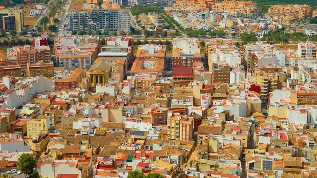 Dense residential district in Spain with colorful apartment blocks and tiled rooftops. Historic urban architecture beside modern housing. Mediterranean city pattern under sunny sky