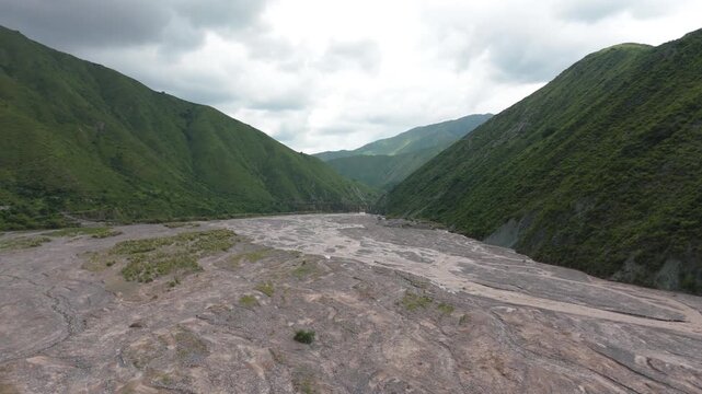 Wide braided river crossing mountain valley near Puente Chorro Blanco, aerial establishing dolly, minimal symmetrical landscape on cloudy day