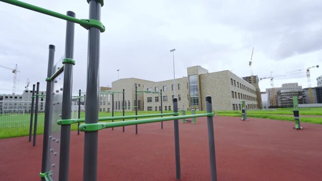 Professional calisthenics station offers equipment for bodyweight training. Overcast sky and urban construction create busy backdrop