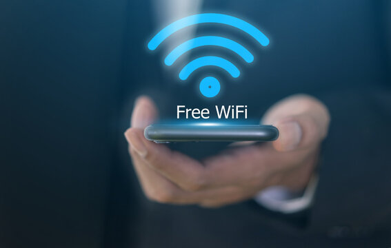 Close up of businessman hand holding smartphone with glowing free wifi network icon. Wireless internet access and digital communication technology concept. Mobile connection