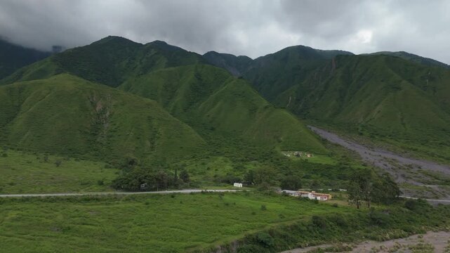 Green mountains and valley near Puente Chorro Blanco beneath storm clouds, aerial wide orbit of road dividing lush landscape near braided river